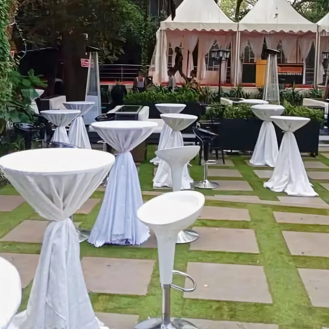 "White spandex dressed bar-height cocktail table with a round top and folding steel base configured for an event layout."
